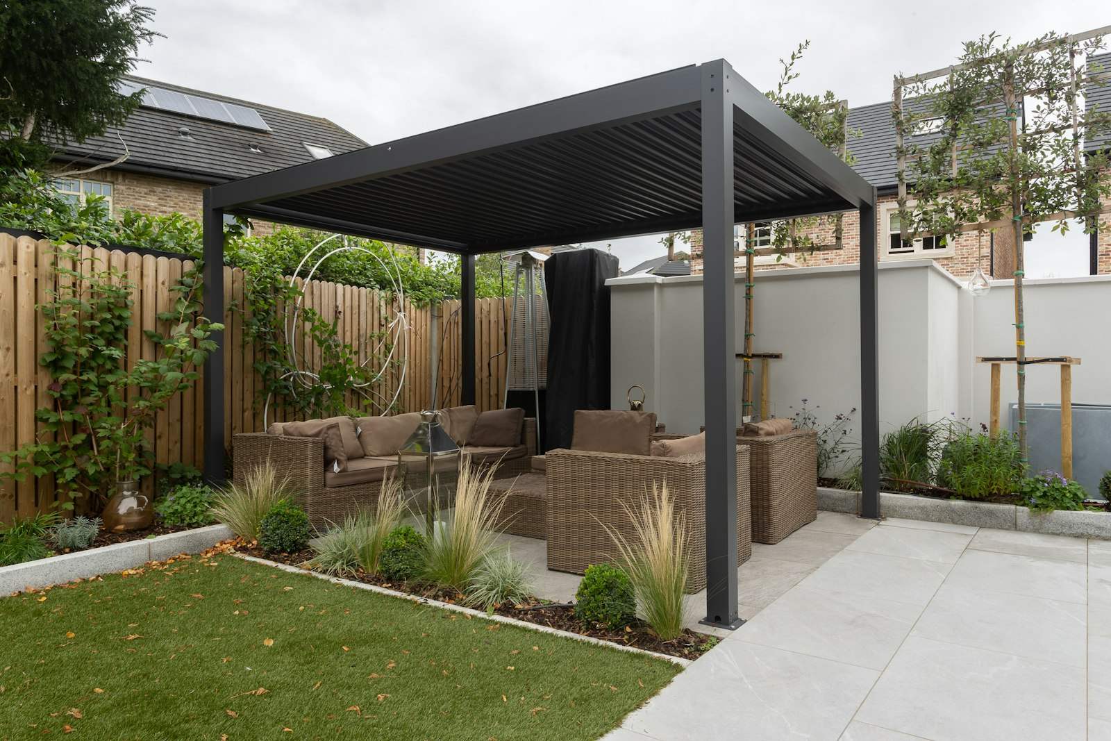 Dark aluminium pergola over garden seating on a paved patio