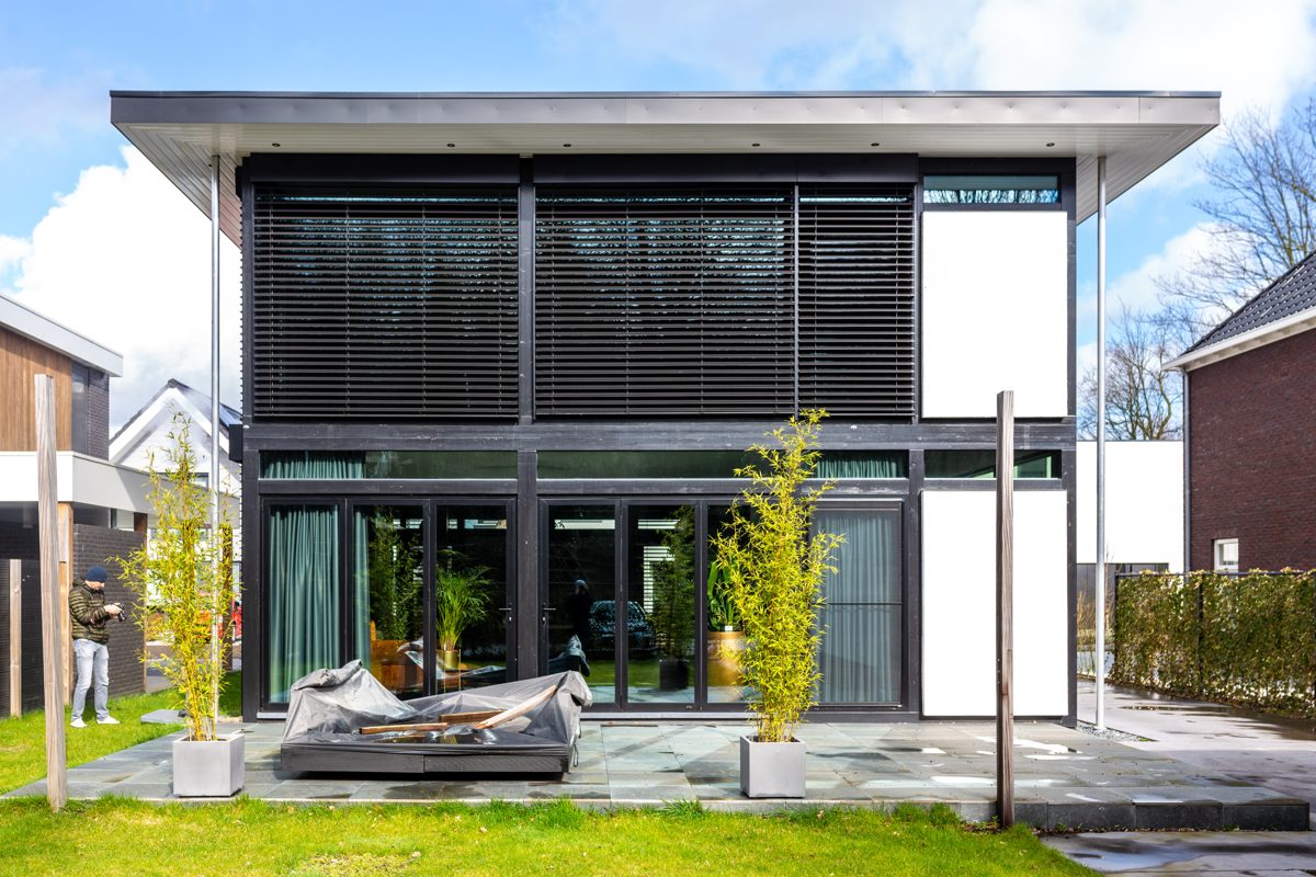 Garden view of a house with black venetian blinds over the upstairs and ground-floor windows
